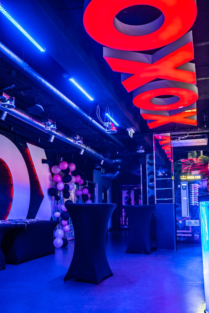 Przygotowane wnętrze klubu z neonowym napisem 'XOXO' pod sufitem, stolikami w czarnych pokrowcach i dekoracją z balonów w odcieniach różu i czerni.