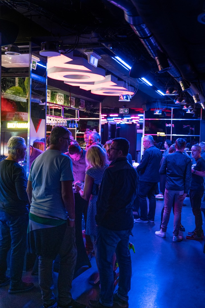 Event firmowy w Warszawie: Grupa ludzi w niebiesko oświetlonym wnętrzu, z widocznym barem w tle i dekoracjami świetlnymi na suficie.