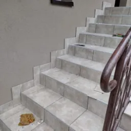 Wyłożone beżowymi płytkami schody zewnętrzne w Chrzanowie, z metalową balustradą, widoczne drobne ślady po pracach glazurniczych oraz okno w tle.