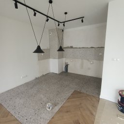 Oleksandr Khalo KHOM-BUD - Wnętrze w trakcie remontu: Połączenie podłogi z lastryko i ułożonego parkietu w jodełkę, widoczne lampy sufitowe na szynach i puszki z farbą.