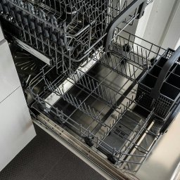 Fachman Damian Fryz - Otwarta, pusta zmywarka z wysuniętymi koszami w nowoczesnej kuchni. Widoczne metalowe kosze na naczynia i sztućce, wnętrze ze stali nierdzewnej.