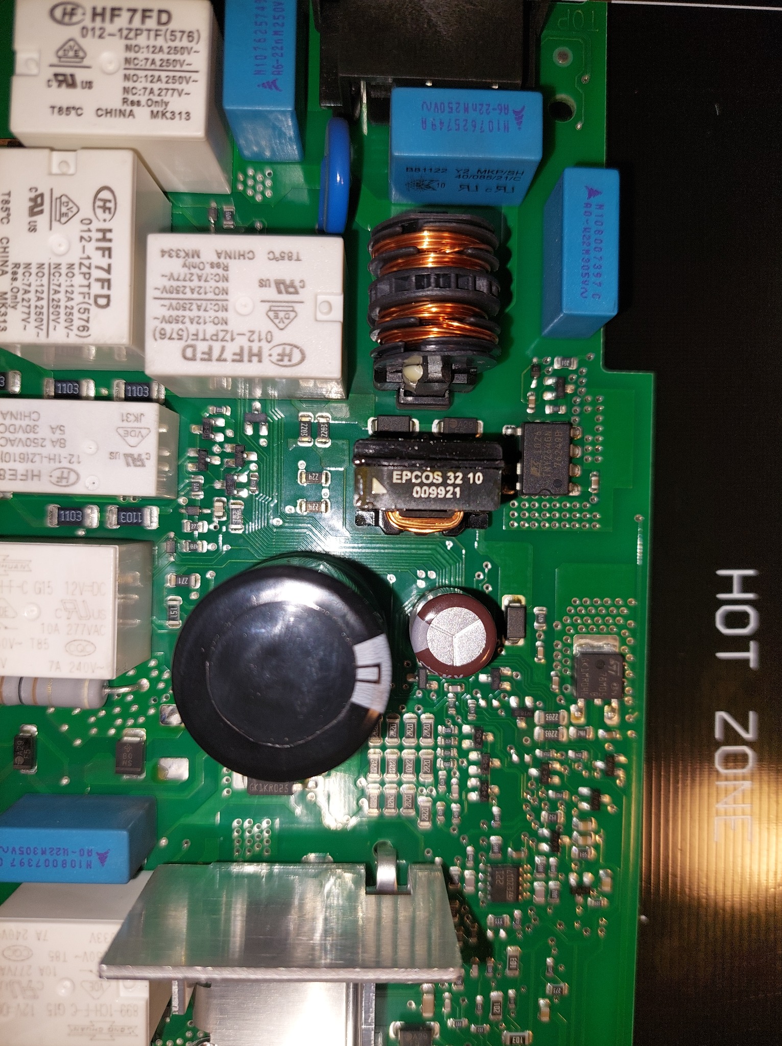 Zielona płytka drukowana z licznymi elementami elektronicznymi, w tym cewki, kondensatory i układy scalone. Widoczne napisy i oznaczenia komponentów.