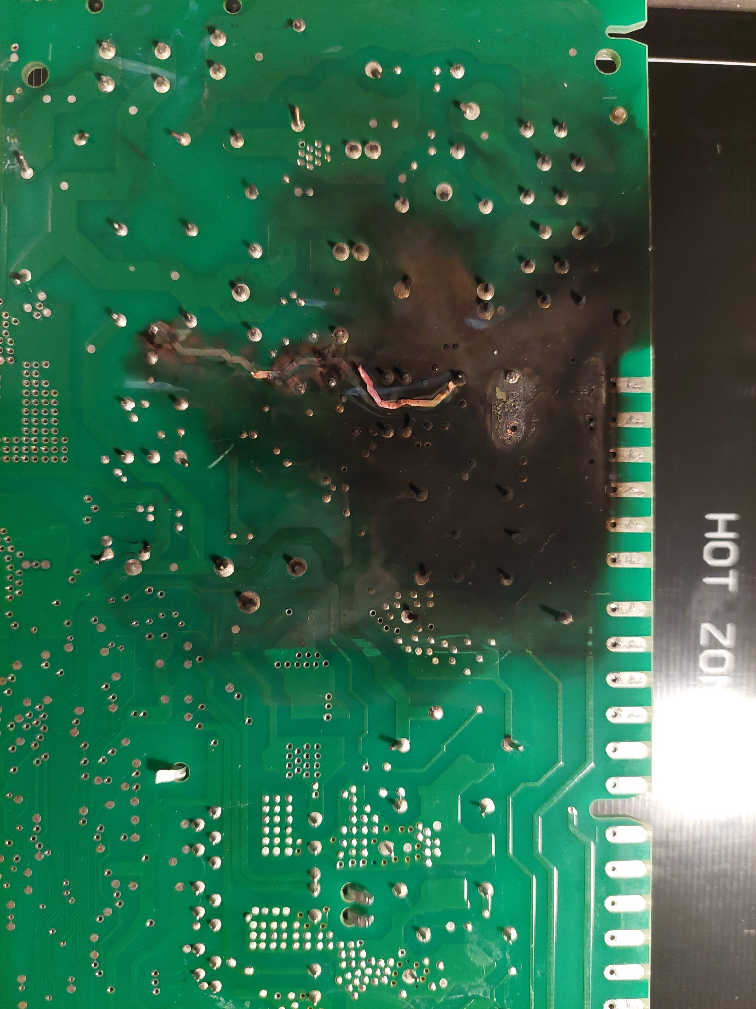 Spalona płyta główna urządzenia AGD z widocznymi śladami zwarcia i osmalenia, ujęcie z bliska, ukazujące uszkodzenia elektroniki.