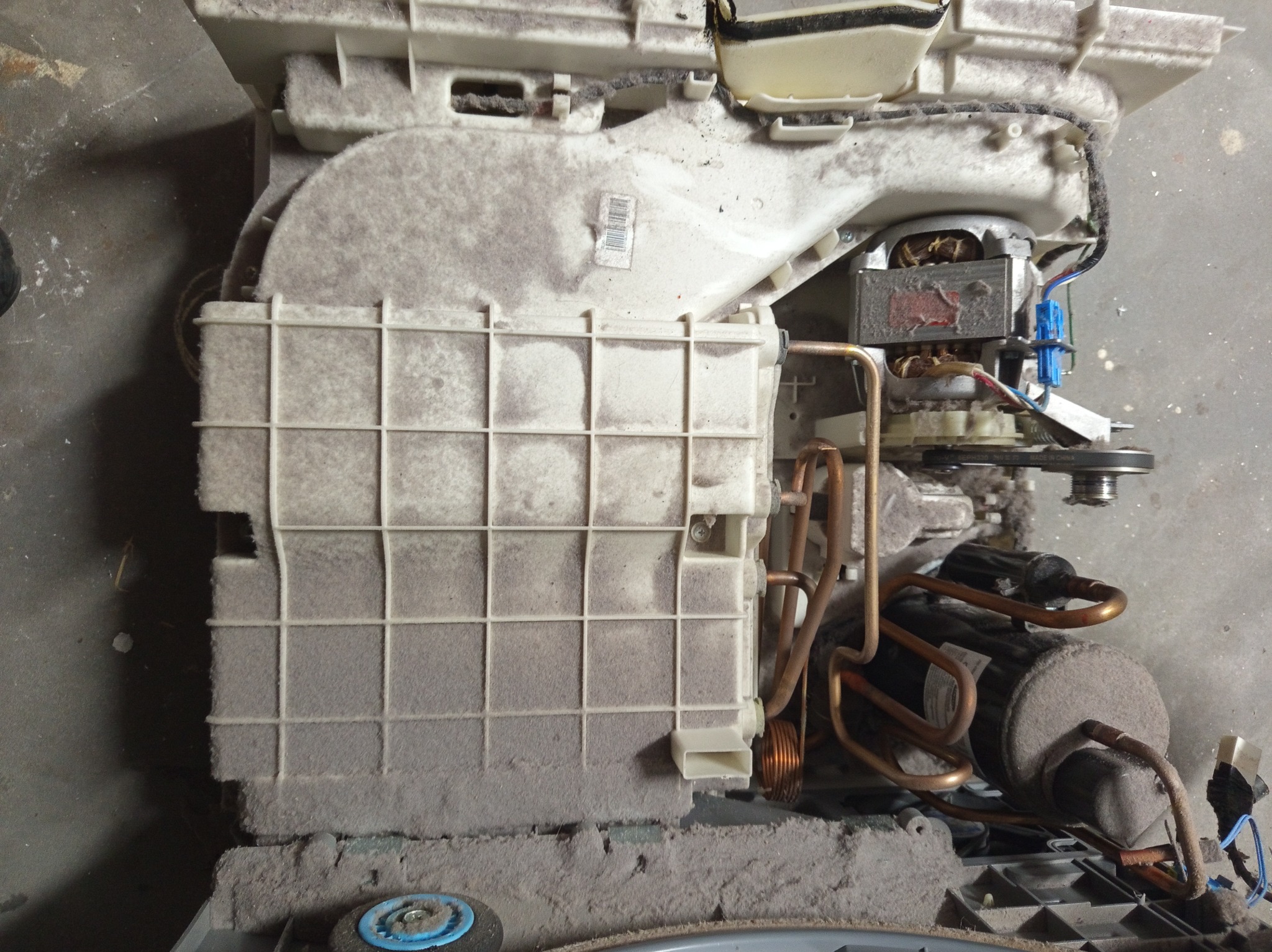 Wnętrze mocno zakurzonej pralki automatycznej z widocznymi elementami grzewczymi, silnikiem i filtrem. Widoczne ślady długotrwałego użytkowania i zaniedbania konserwacji.