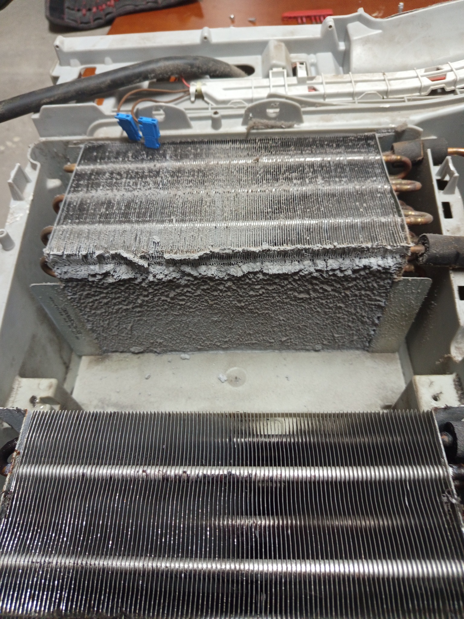 Zanieczyszczona, rozmontowana chłodnica urządzenia AGD z widocznymi warstwami kurzu i brudu na lamelach, ukazująca stopień zużycia i potrzebę serwisu.