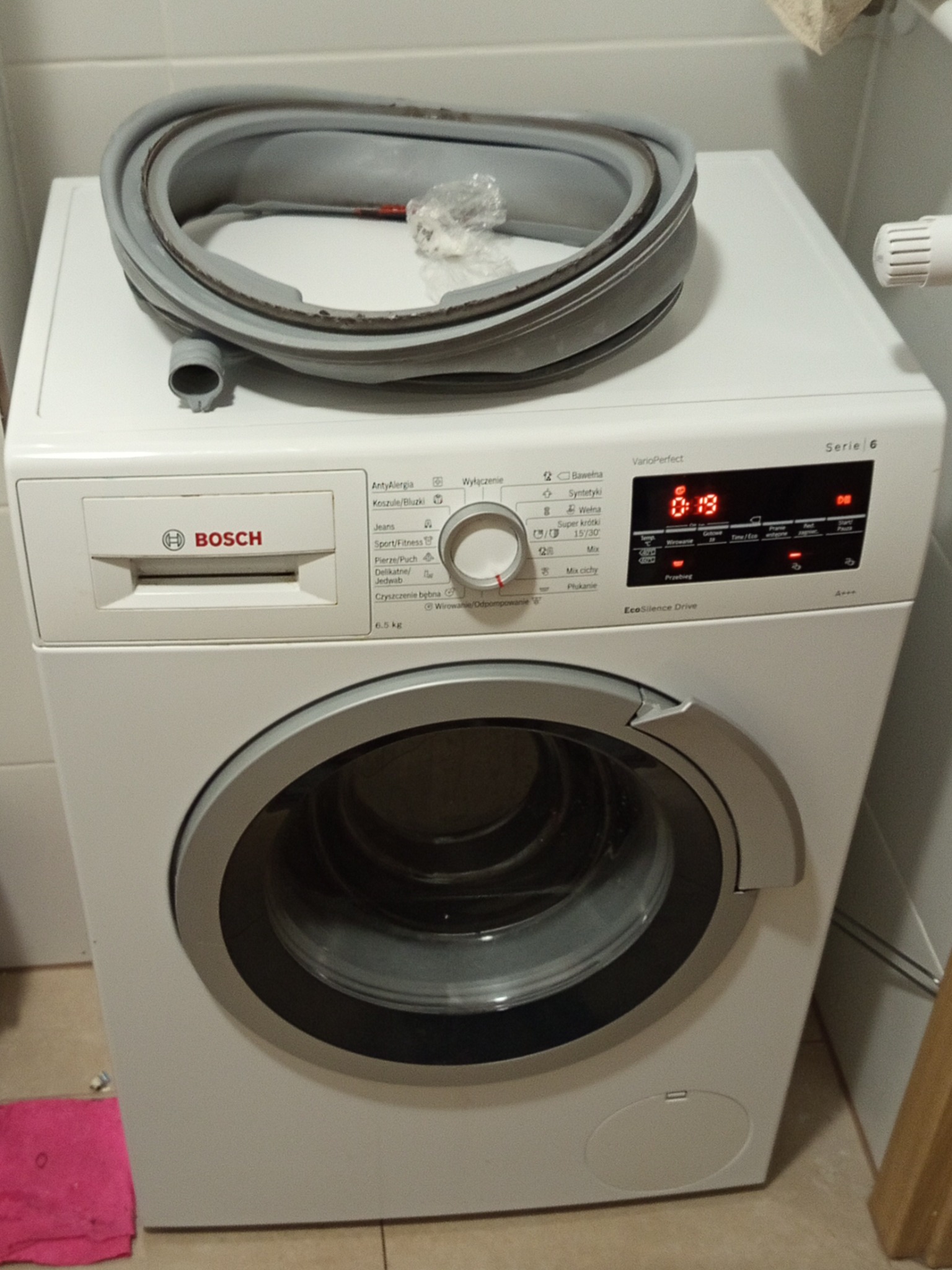 Biała pralka Bosch Serie 6 z otwartą uszczelką kołnierza na górze, sugerująca naprawę lub wymianę. Widoczny panel sterowania i wyświetlacz czasu.