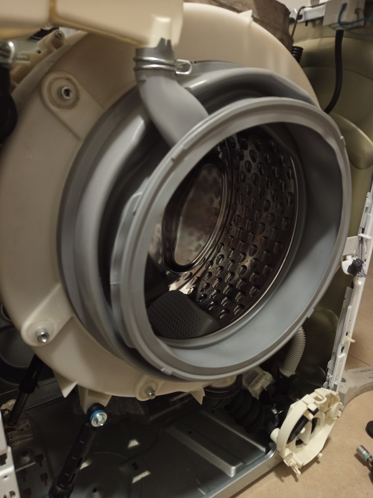 Rozłożona pralka z widocznym bębnem i elementami konstrukcyjnymi. Gumowy kołnierz uszczelniający bęben. Widoczne ślady demontażu, narzędzia w tle.