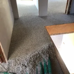 Poddasze w trakcie ocieplania granulatem, widoczne zielone węże do wdmuchiwania materiału izolacyjnego i tymczasowe zabezpieczenie schodów płytą OSB.