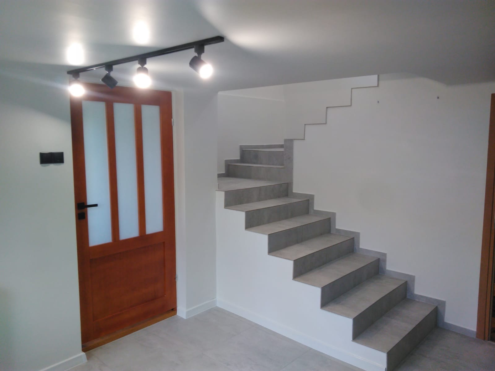 Wnętrze: drewniane drzwi z szybami, schody wyłożone szarymi płytkami, oświetlenie szynowe z czterema reflektorami.
