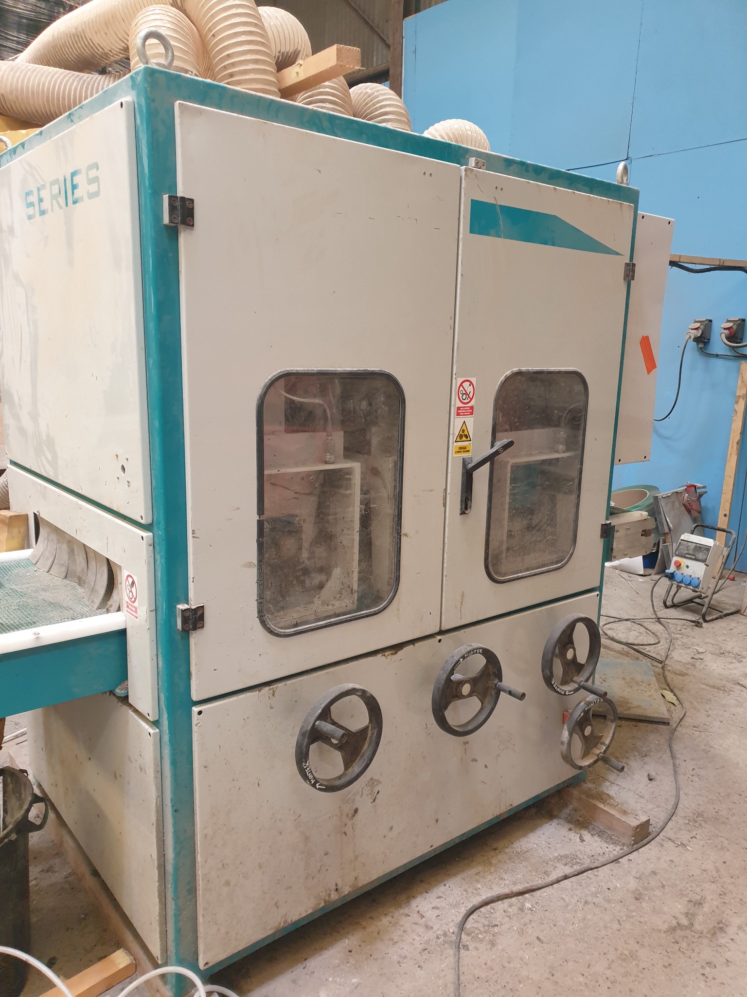 Duża, używana szlifierka szerokotaśmowa z czterema pokrętłami regulacyjnymi i widocznymi przewodami wentylacyjnymi na górze.