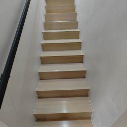 RENO-PAR VADYM SHPITSA - Jasne drewniane schody z czarną metalową balustradą, widok z dołu, ściany w odcieniach beżu.