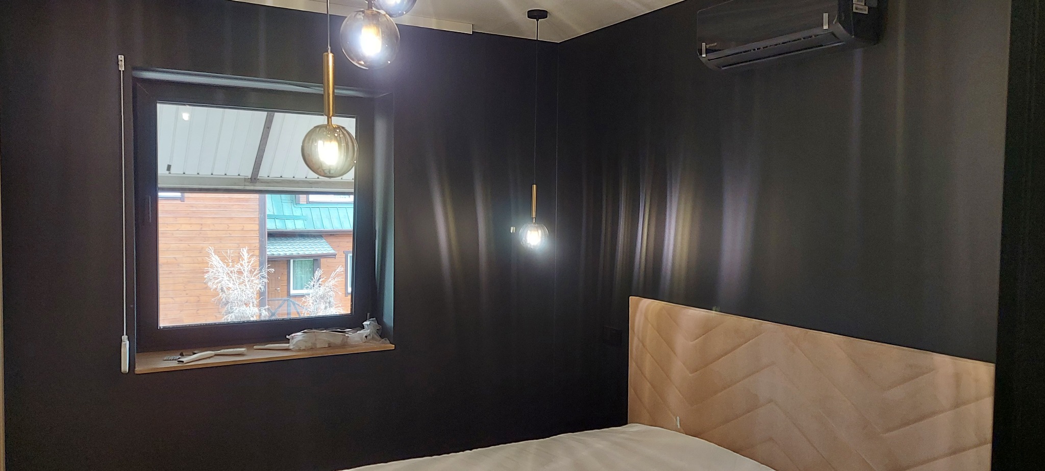 Nowoczesna sypialnia z czarnymi ścianami, oświetleniem punktowym i dekoracyjną, beżową ramą łóżka w jodełkę, klimatyzacja na ścianie.