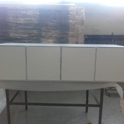 Weld Lab Pro usługi ślusarsko-spawalnicze KAROLINA WOJTECKA - Biała szafka wisząca z czterema drzwiczkami, umieszczona na metalowym stole w warsztacie, z widocznymi materiałami budowlanymi w tle.