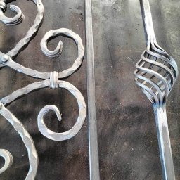 Weld Lab Pro usługi ślusarsko-spawalnicze KAROLINA WOJTECKA - Elementy dekoracyjne z metalu, prawdopodobnie fragment balustrady lub bramy, z widocznymi spawami i spiralnym zdobieniem, leżące na roboczym, metalowym stole.