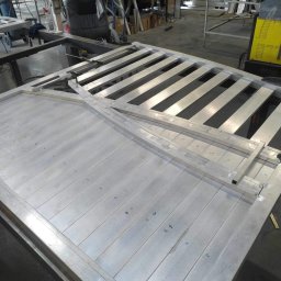 Weld Lab Pro usługi ślusarsko-spawalnicze KAROLINA WOJTECKA - Wnętrze warsztatu z widoczną konstrukcją metalową bramy wjazdowej w trakcie spawania, z numerami naniesionymi na elementach, spawarka w tle.