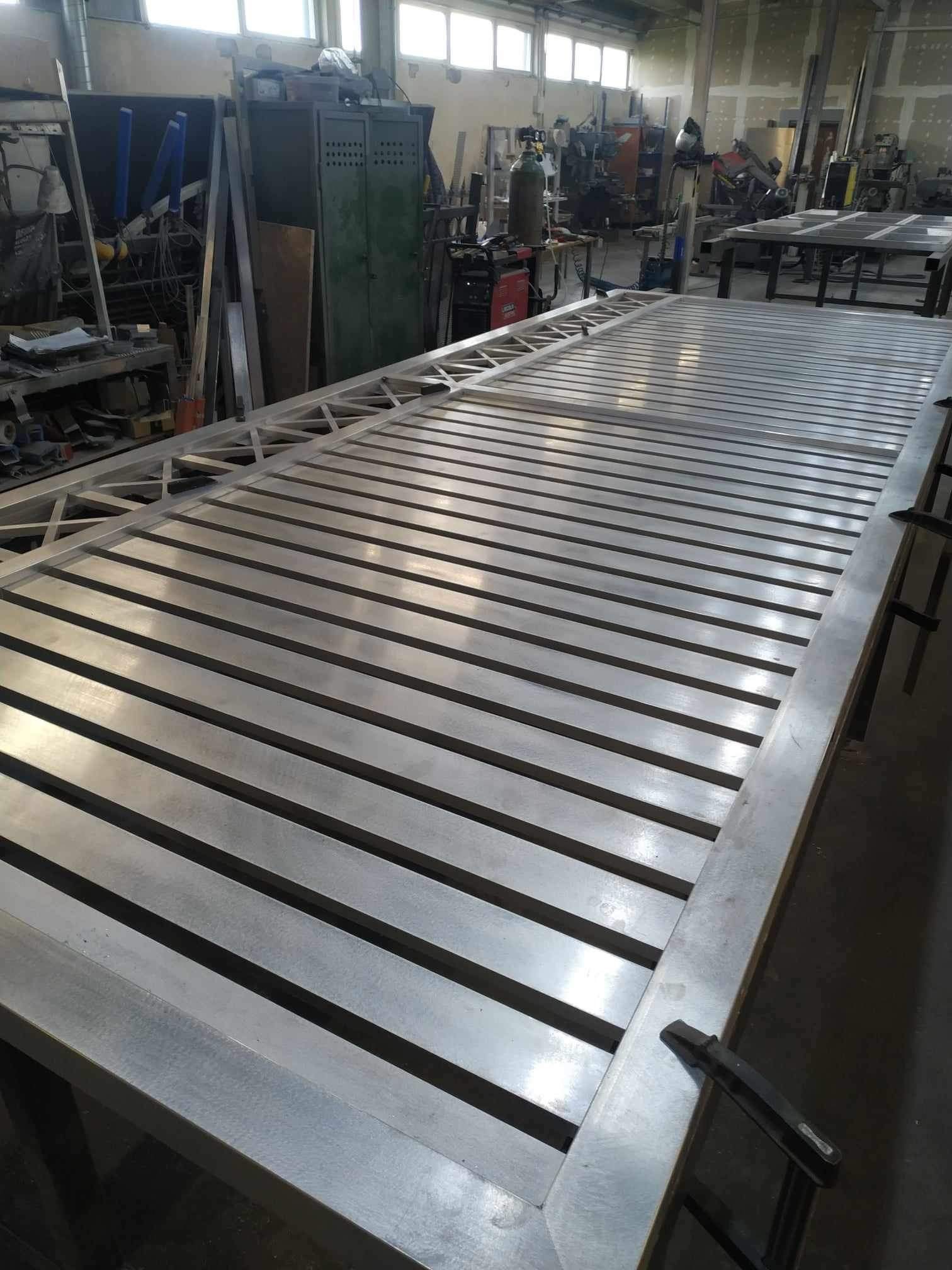 Konstrukcja bramy z profili metalowych, w trakcie spawania, widoczne złącza i elementy mocujące, w tle warsztat ślusarski.