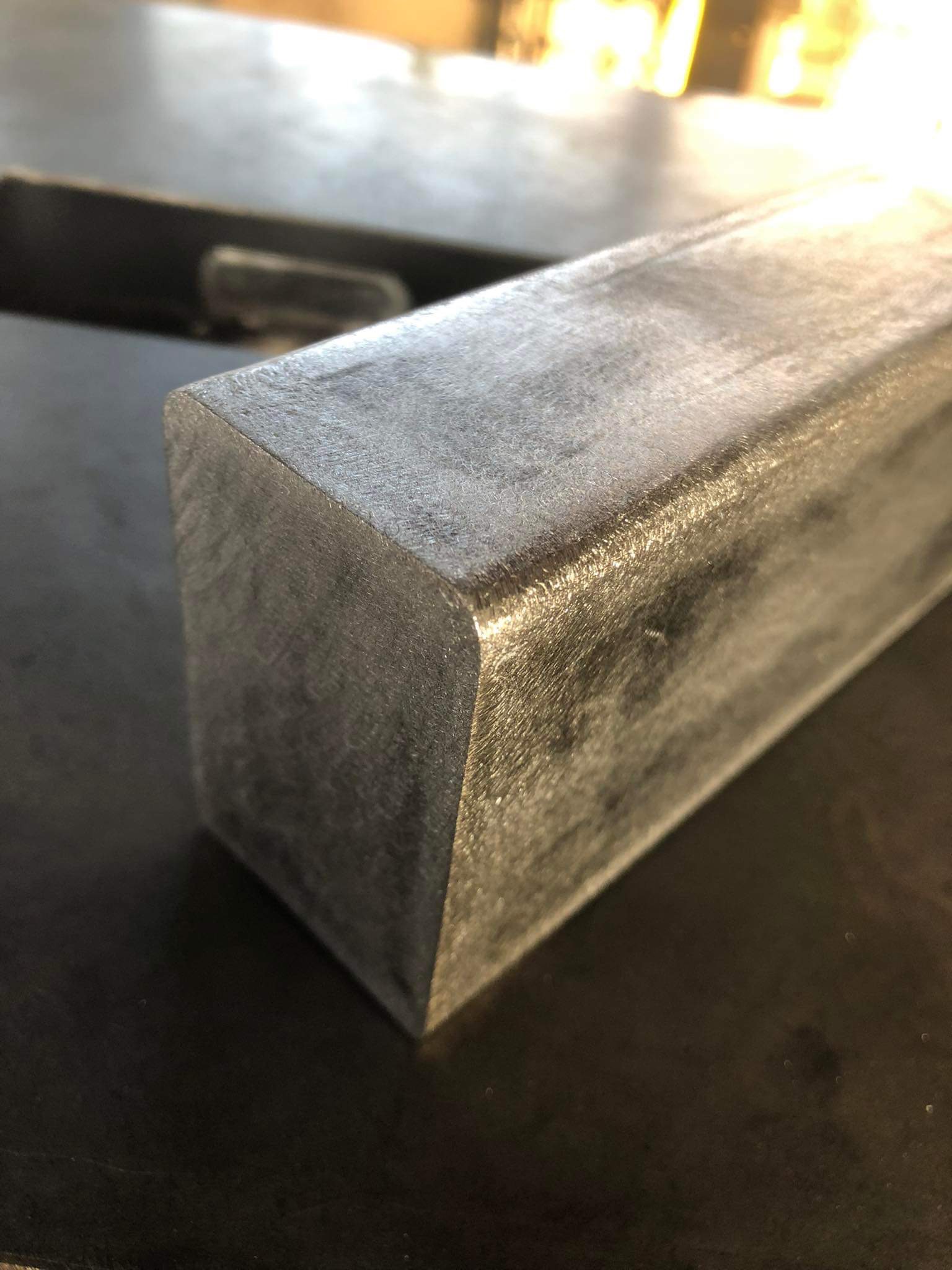 Szlifowany, stalowy profil kwadratowy z zaokrąglonymi krawędziami leżący na ciemnym blacie, widoczne ślady obróbki.