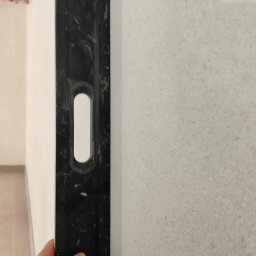 BoTom Tomasz Bogusz - Sprawdzanie pionu ściany za pomocą poziomicy. Widoczna struktura ściany i fragment instalacji pod sufitem. Ręka przytrzymuje narzędzie.