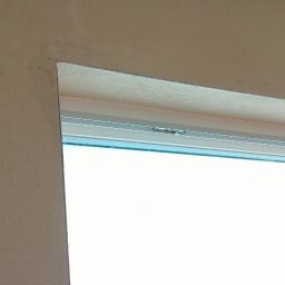 BoTom Tomasz Bogusz - Fragment ściany z oknem po nałożeniu tynku. Widoczne nierówności na suficie i ścianie. Okno białe, plastikowe. Na zewnątrz widoczny zimowy krajobraz.