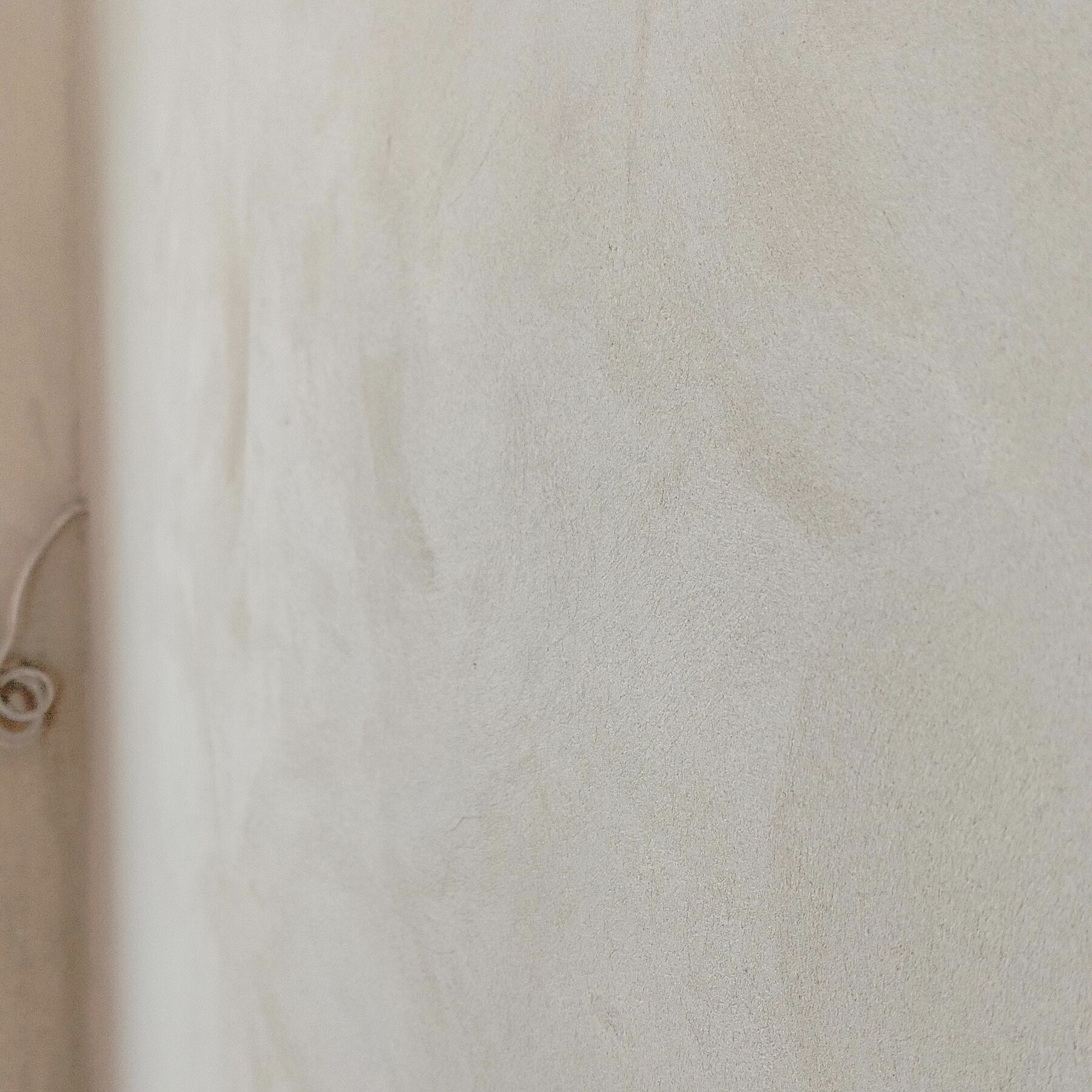 Jasnoszara, gładka ściana z delikatną fakturą, oświetlona z lewej strony, z widocznym fragmentem zwiniętego kabla w rogu. Minimalistyczne wykończenie wnętrza.