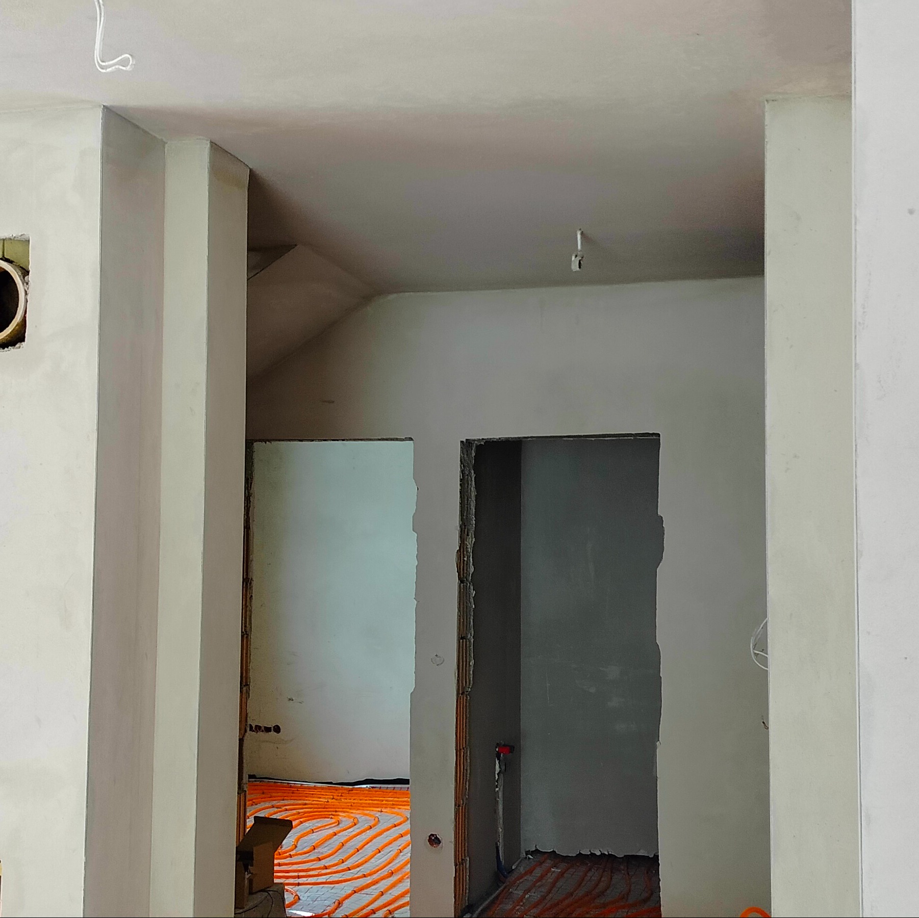 Wnętrze w trakcie prac wykończeniowych: widoczne ściany po szpachlowaniu, przygotowane podłoże pod ogrzewanie podłogowe z pomarańczowymi rurami. Surowy stan.