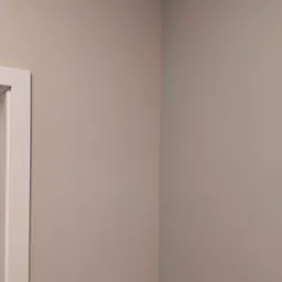 Świeżo pomalowany narożnik pokoju w odcieniach beżu, widoczna biała framuga drzwi po lewej stronie.