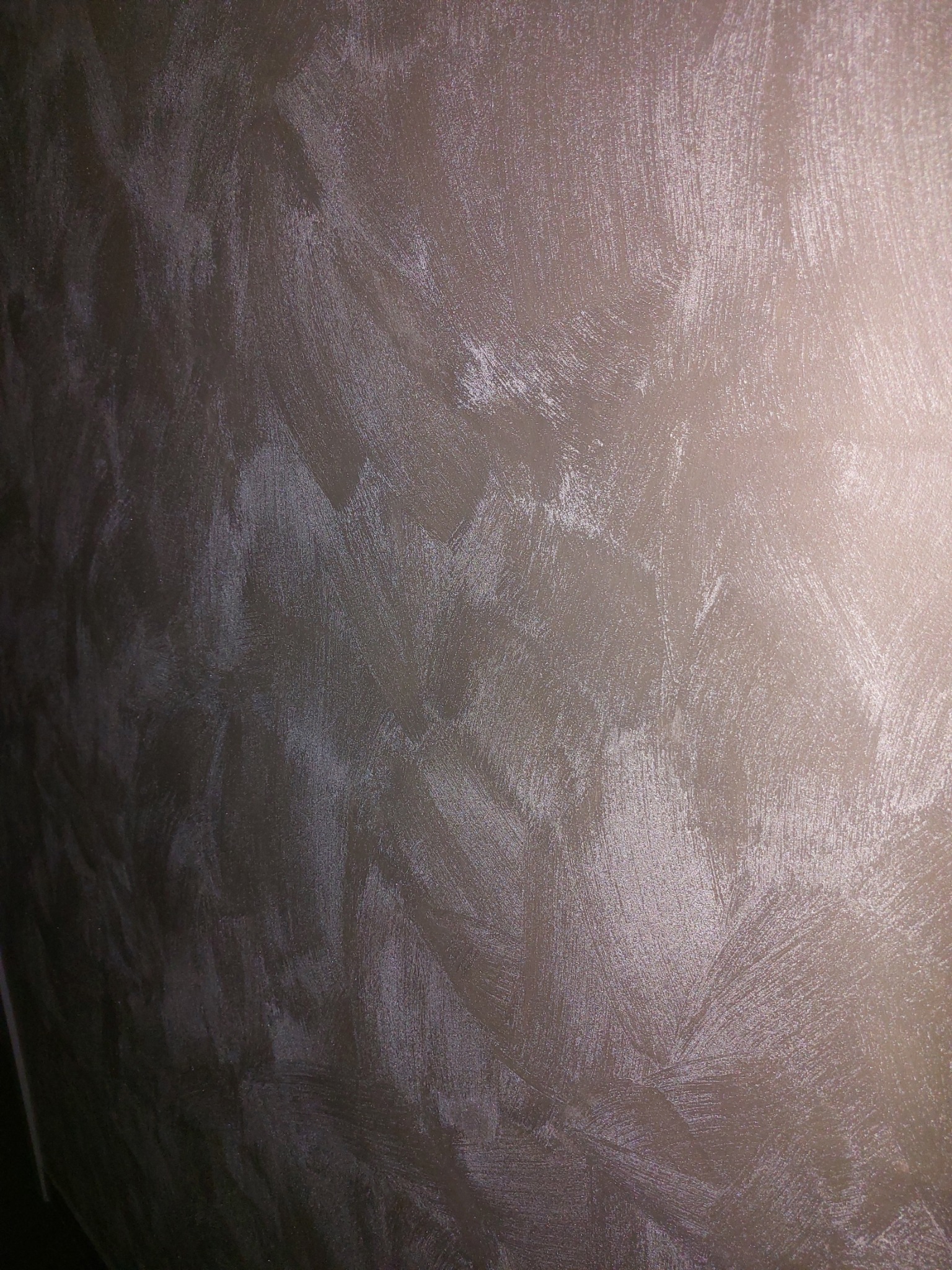 Ściana z efektem dekoracyjnym w odcieniach beżu i brązu, widoczne ślady pędzla tworzące unikalną fakturę, oświetlenie z prawej strony podkreśla nierówności powierzchni.