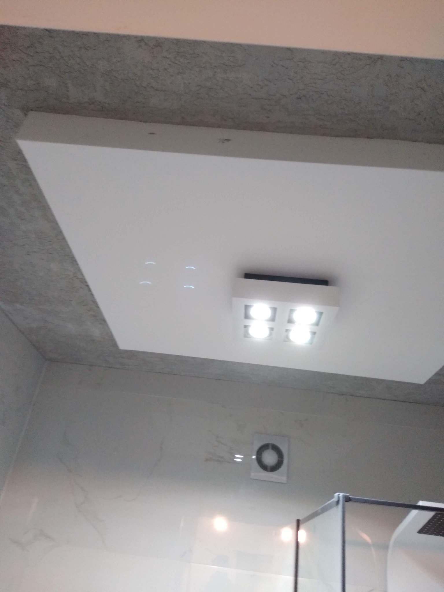 Podwieszany sufit z oświetleniem LED w łazience, widoczny fragment kabiny prysznicowej i wentylator sufitowy.