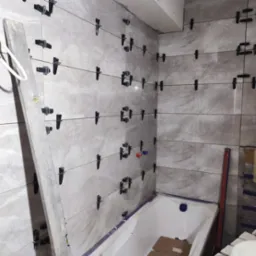 Montaż szarych płytek w łazience z użyciem klipsów poziomujących i krzyżyków dystansowych, widoczna wanna i poziomica.