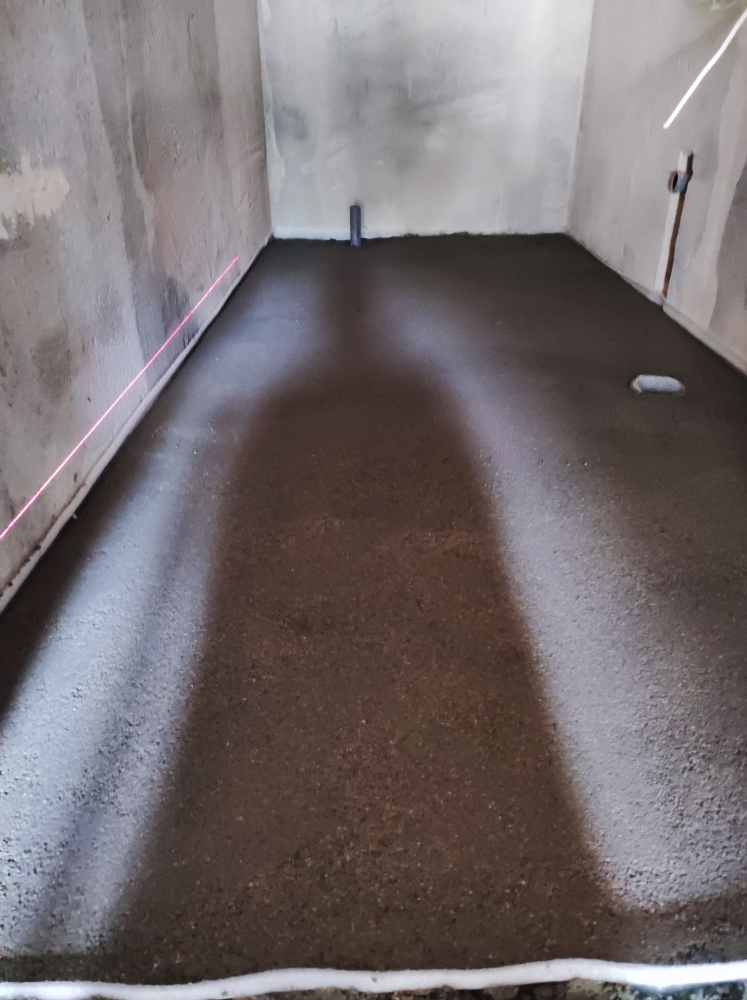 Wyrównana, mokra wylewka podłogowa w surowym wnętrzu, wyznaczona poziomnicą laserową.