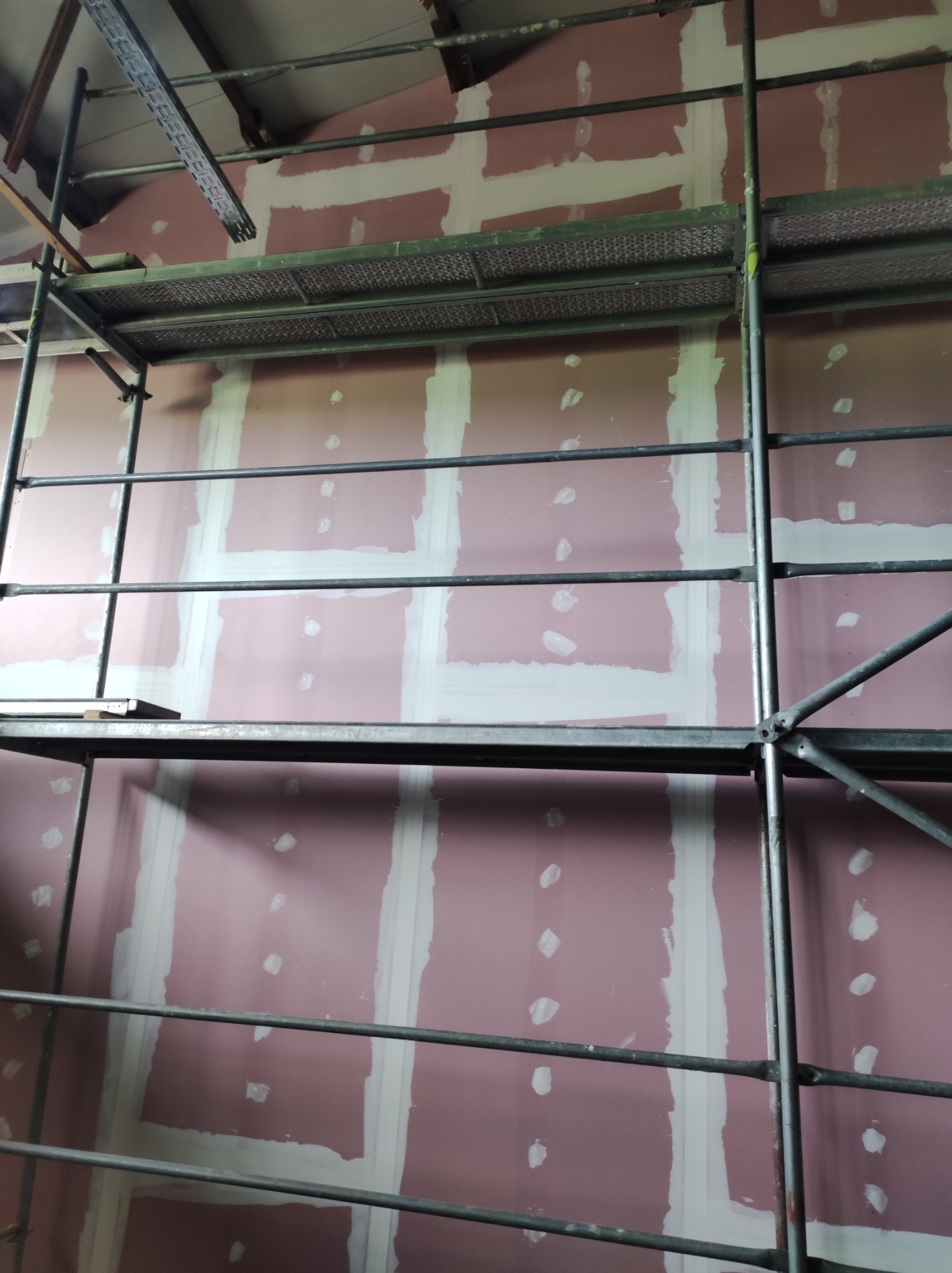 Ściana z płyt kartonowo-gipsowych w trakcie szpachlowania łączeń, widoczne rusztowanie.