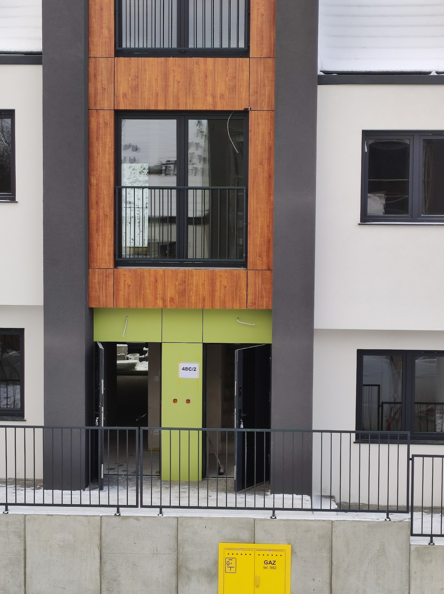 Nowoczesny budynek wielorodzinny w trakcie wykończenia, z elementami drewnopodobnymi i świeżo pomalowanym na jasnozielono wejściem do lokalu 48C/2.