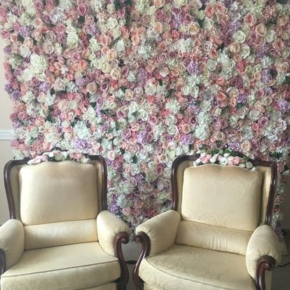 Dwa kremowe fotele ustawione przed ścianą z różnokolorowych kwiatów, tworzących dekoracyjną ściankę.