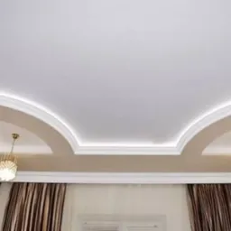 Dekoracyjny sufit podwieszany z oświetleniem LED, wykończony sztukaterią i dwoma złotymi lampami wiszącymi, w tle zasłony w brązowe pasy.