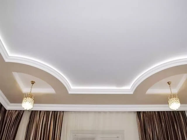 Dekoracyjny sufit podwieszany z oświetleniem LED, wykończony sztukaterią i dwoma złotymi lampami wiszącymi, w tle zasłony w brązowe pasy.