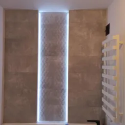 Wykończona łazienka z podświetlaną wnęką z dekoracyjnymi płytkami, grzejnik drabinkowy i czarna armatura.