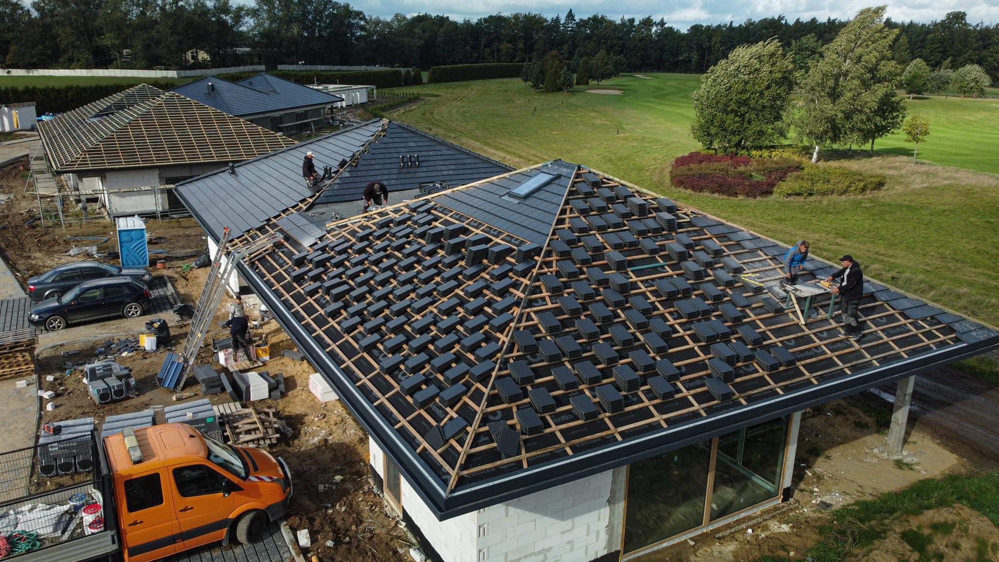 Montaż dachówki ceramicznej na nowym domu w Wejherowie, widok z góry na częściowo pokryty dach z widoczną konstrukcją drewnianą i ekipą dekarzy pracującą na dachu.