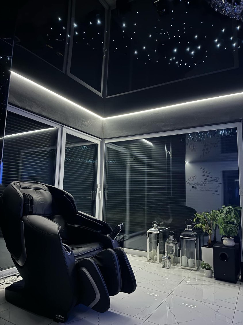 Pokój z czarnym fotelem masującym, sufitem imitującym gwiaździste niebo, oświetleniem LED i lampionami dekoracyjnymi.
