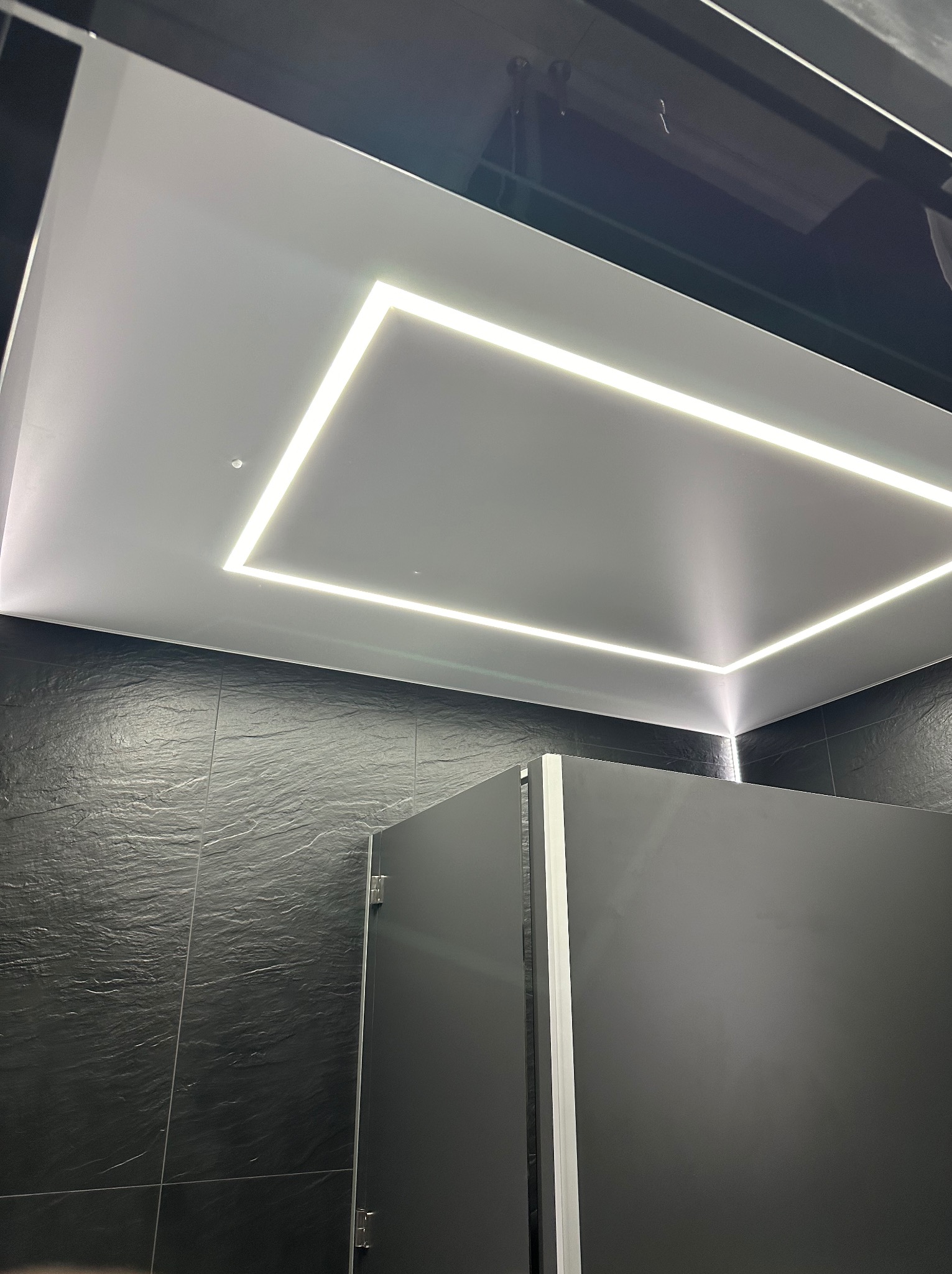 Nowoczesna łazienka z czarną, łupkową ścianą i podwieszanym sufitem z wbudowanym oświetleniem LED w kształcie prostokąta.