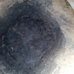 Głęboki wykop w ziemi, widoczna ciemna gleba i fragment betonowego obrzeża.