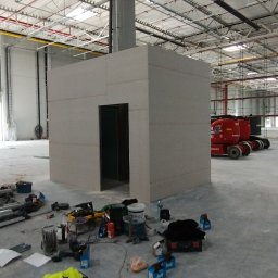 Łukasz Gabrys - Budowa pomieszczenia z płyt karton gips w hali przemysłowej w Ksawerowie, widoczne narzędzia i materiały budowlane, podnośnik koszowy w tle.