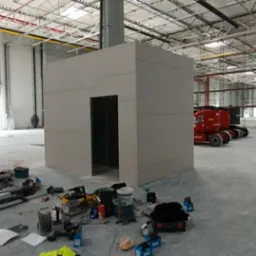 Budowa pomieszczenia z płyt karton gips w hali przemysłowej w Ksawerowie, widoczne narzędzia i materiały budowlane, podnośnik koszowy w tle.