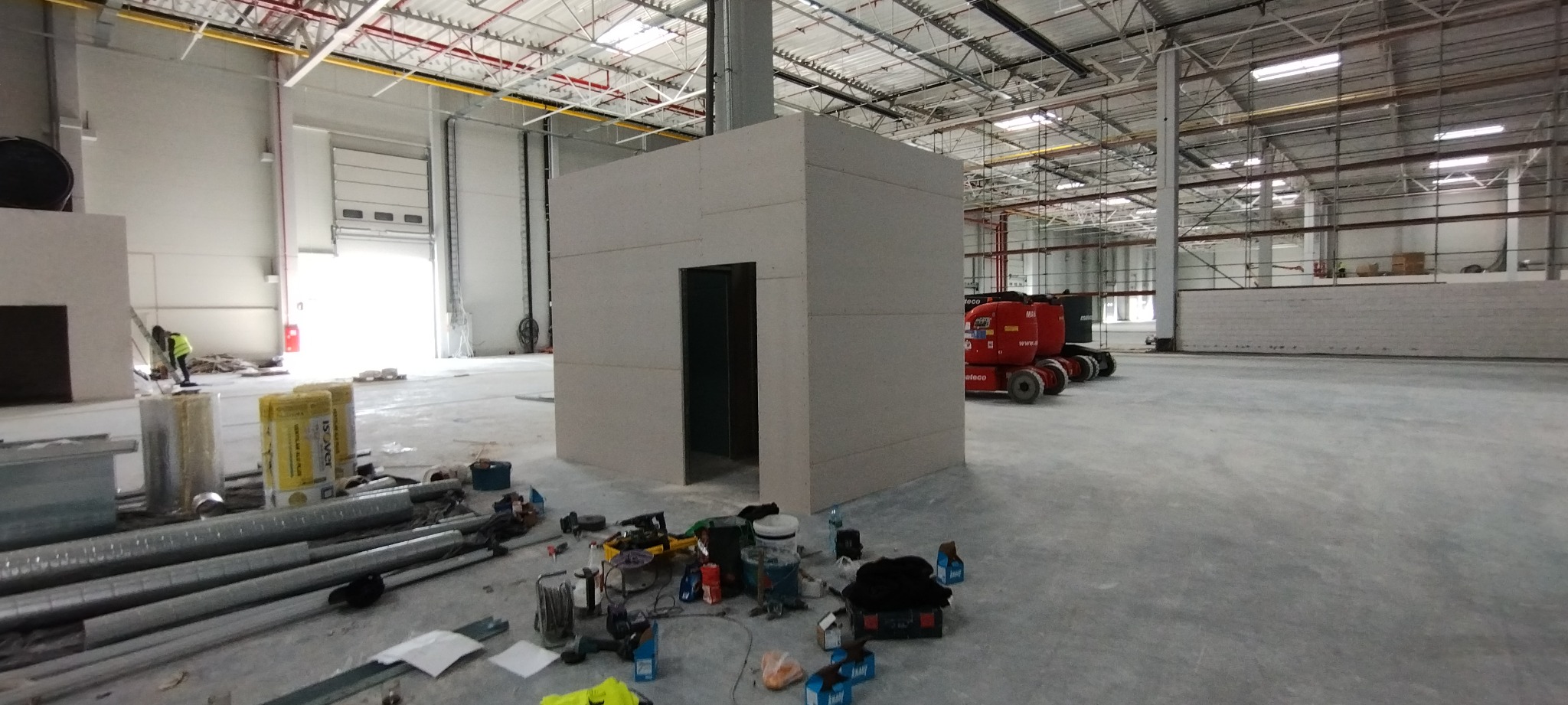 Budowa pomieszczenia z płyt karton gips w hali przemysłowej w Ksawerowie, widoczne narzędzia i materiały budowlane, podnośnik koszowy w tle.