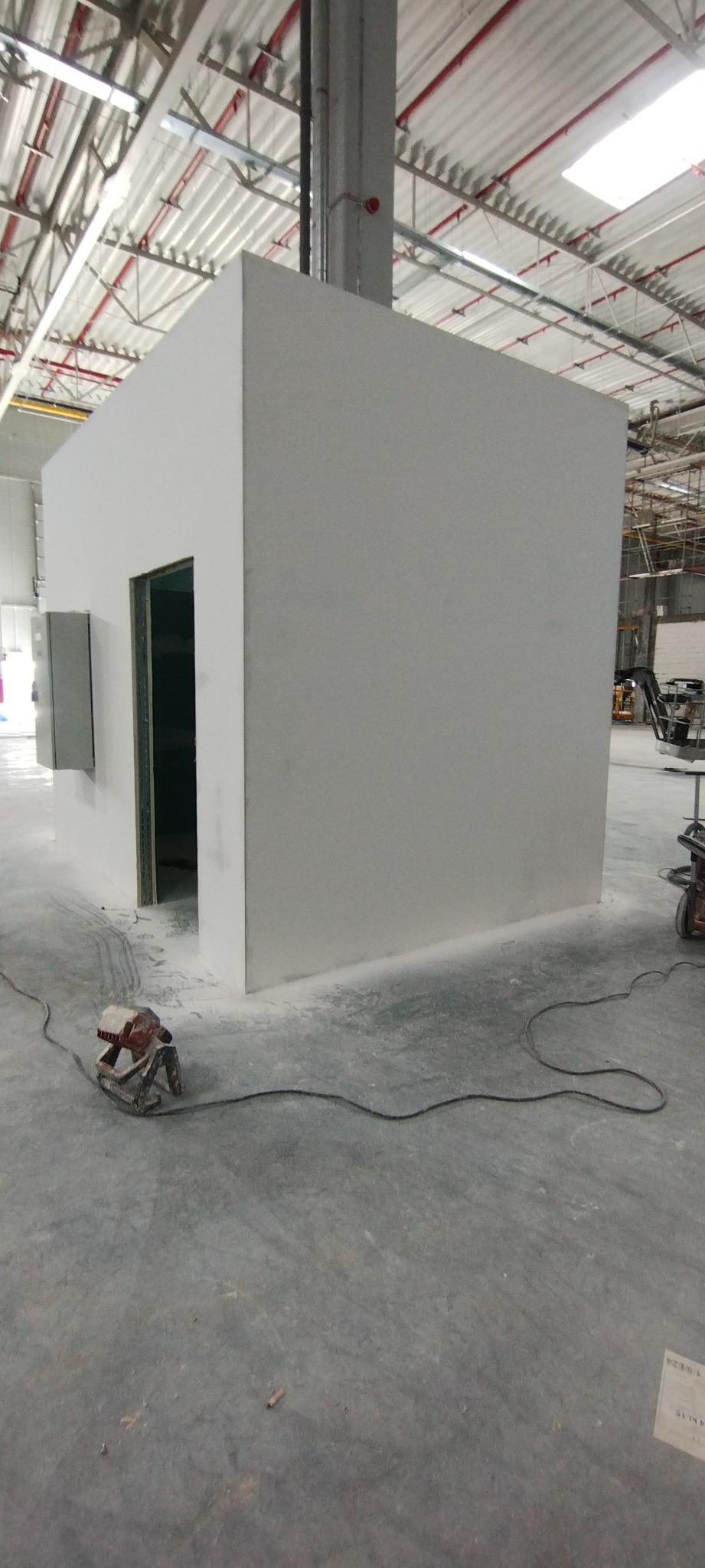 Wnętrze hali produkcyjnej z wygłuszoną, pomalowaną na biało kabiną z otwartymi drzwiami i szarym panelem na ścianie, szlifierka przy podłodze, widoczne ślady pyłu po szlifowaniu.