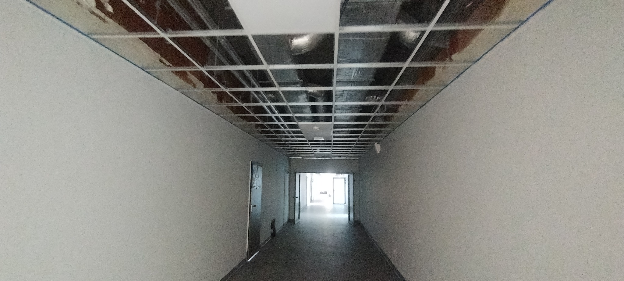 Korytarz w trakcie prac wykończeniowych, widoczna metalowa konstrukcja sufitu podwieszanego i świeżo pomalowane ściany na szaro.