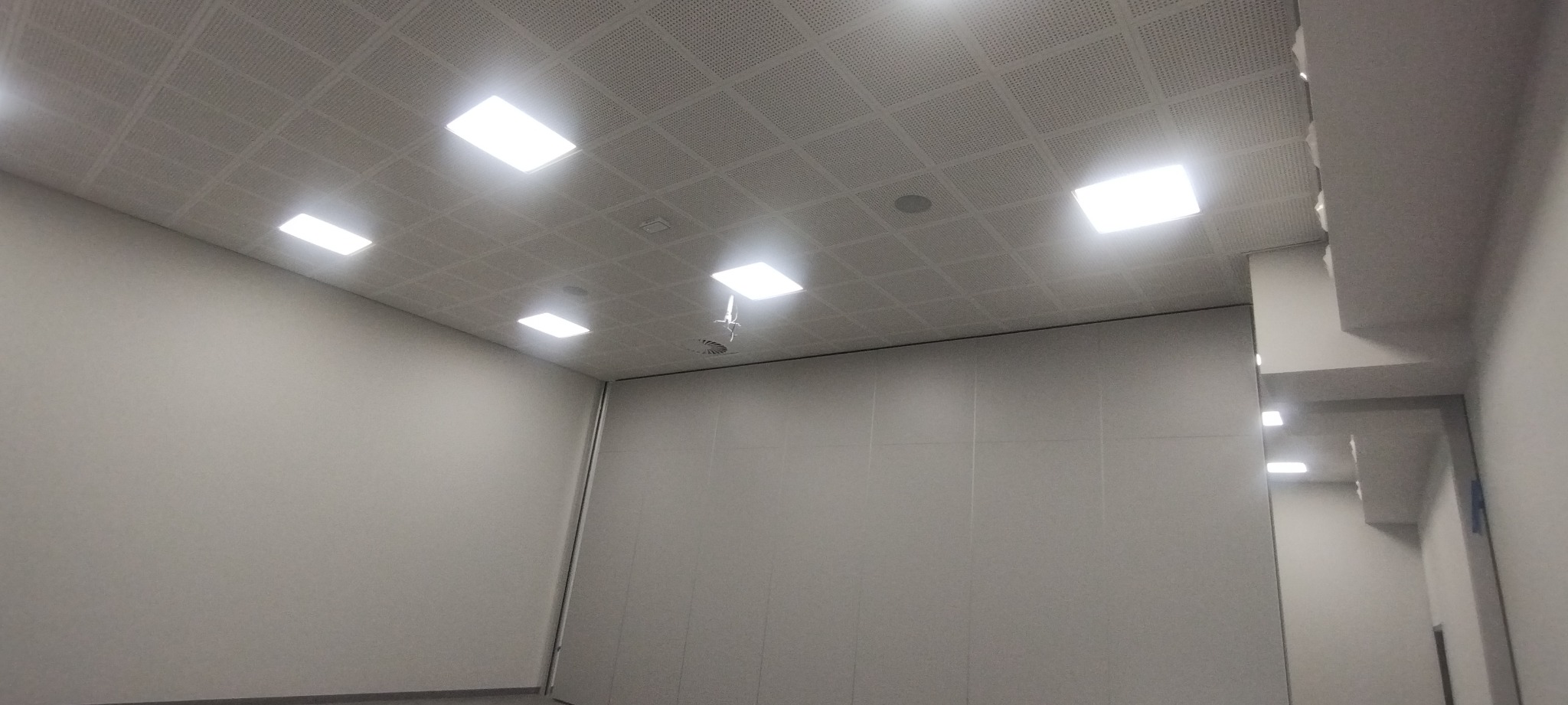 Białe panele sufitowe z wbudowanymi kwadratowymi lampami LED w pomieszczeniu z gładkimi, jasnymi ścianami.