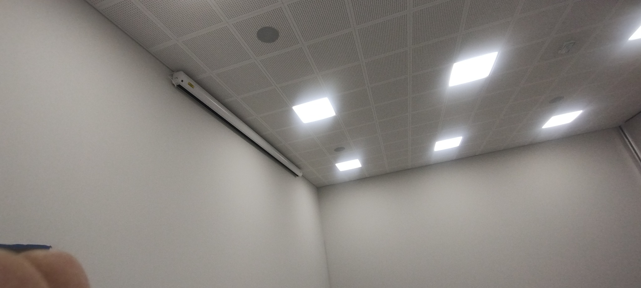 Wnętrze biura z zamontowanym sufitem podwieszanym z oświetleniem LED i zwiniętym ekranem projekcyjnym na ścianie.