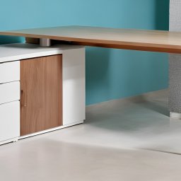 KROYEE Sp. z o.o. - Nowoczesne biurko z jasnego drewna z trzema nogami, połączone z białą szafką z trzema szufladami i drewnianymi drzwiczkami, na tle turkusowej i szarej ściany.