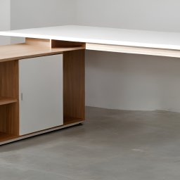 KROYEE Sp. z o.o. - Nowoczesne biurko narożne z blatem w kolorze białym i drewnianą szafką z półkami, wsparte na skośnych nogach z jasnego drewna.