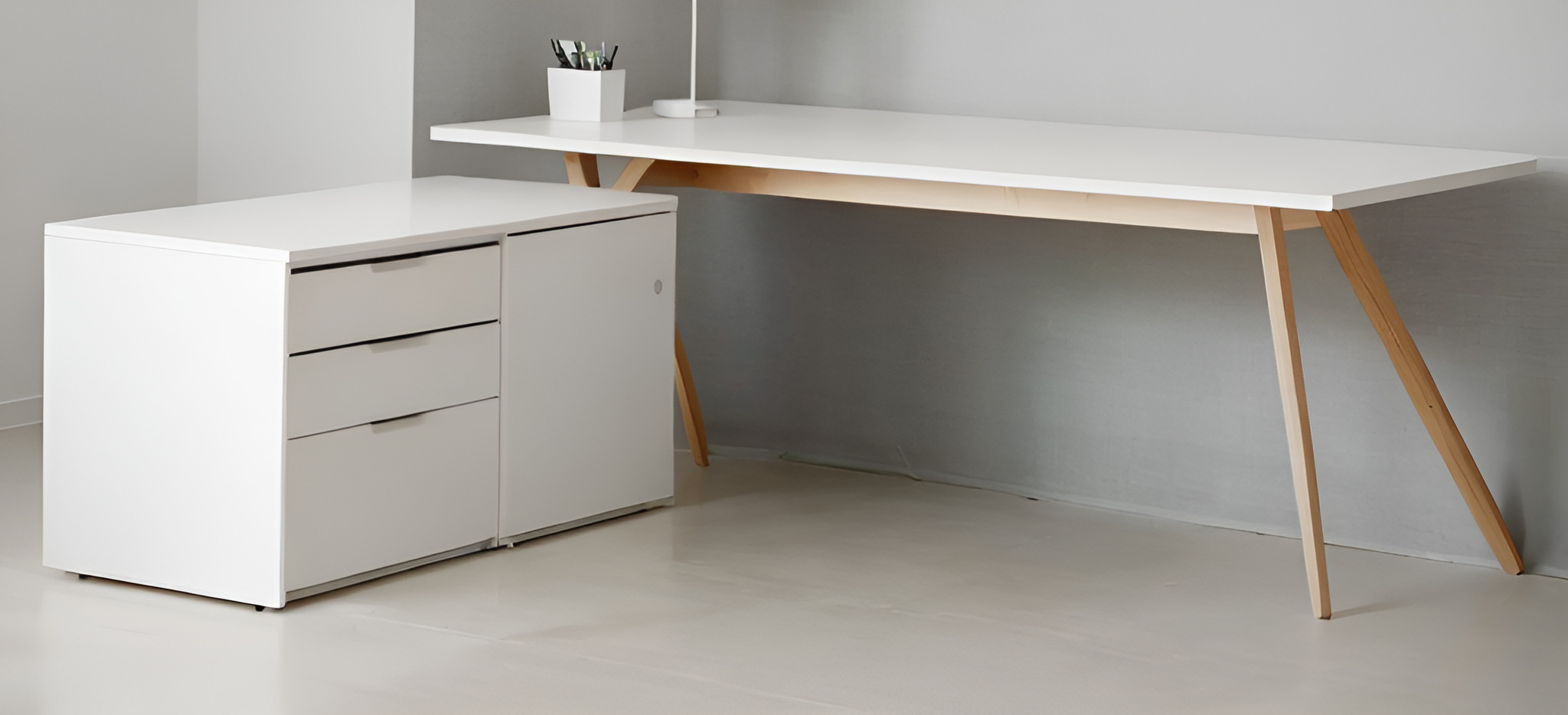 Minimalistyczne, białe biurko z drewnianymi nogami i szafką z trzema szufladami w jasnym, nowoczesnym wnętrzu.